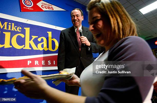 Republican presidential hopeful and former Arkansas governor Mike Huckabee laughs as a waitress walks in front of him carrying a pizza as he speaks...
