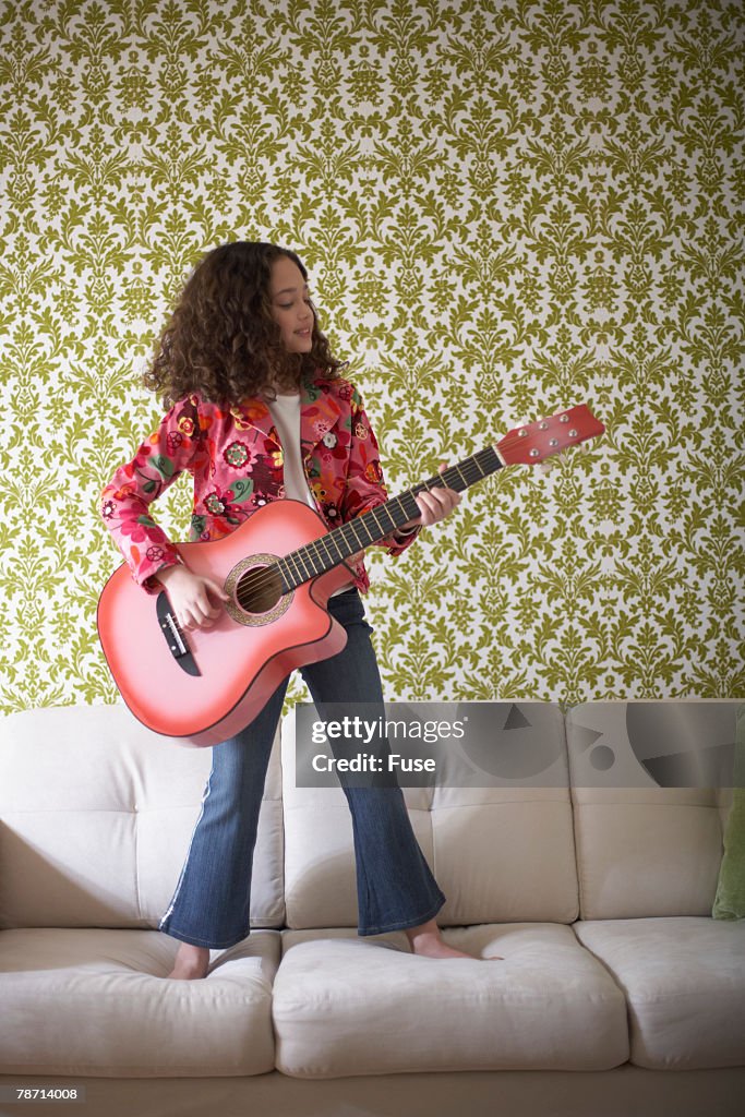 Girl Standing on Sofa Playing a Guitar