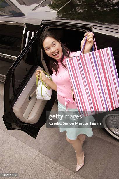 excited young woman in front of limousine, proudly holding up her shopping bag - limousine stock pictures, royalty-free photos & images