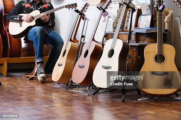 man playing guitar in store by displays - guitar shop stock pictures, royalty-free photos & images
