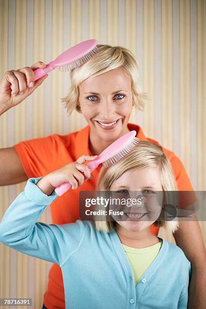 mother and daughter brushing their hair - brushing hair stock-fotos und bilder