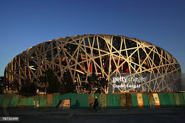 Worker rides a bicycle at sunset at the construction site of the National Stadium, the main stadium of Beijing Olympic Games on January 3, 2008 in...