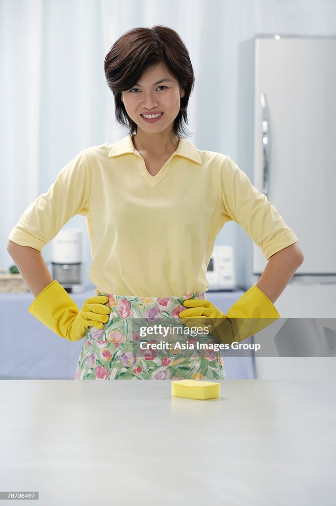 Woman in kitchen, wearing gloves and apron, hands on hips