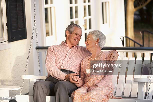 senior couple together on their porch - swing chair stock pictures, royalty-free photos & images