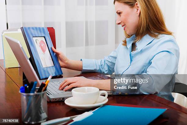 businesswoman looking at framed photograph on her desk - picture frame desk stock pictures, royalty-free photos & images