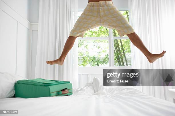 energized young man jumping on hotel bed - floating bed stock pictures, royalty-free photos & images