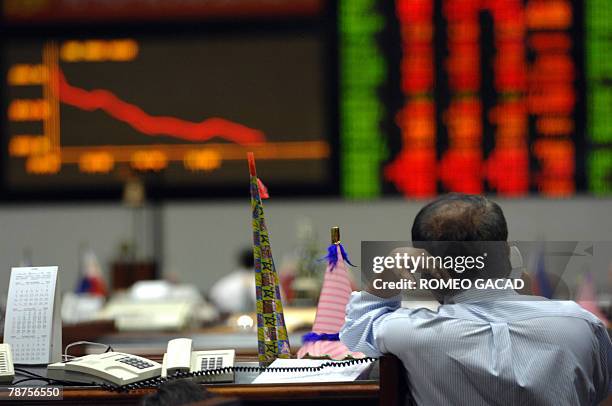 Trader leans on a divider with a New Years cardboard trumpet as he looks at the dislay board of the Philippine Stock Exchange in Manila 03 January...