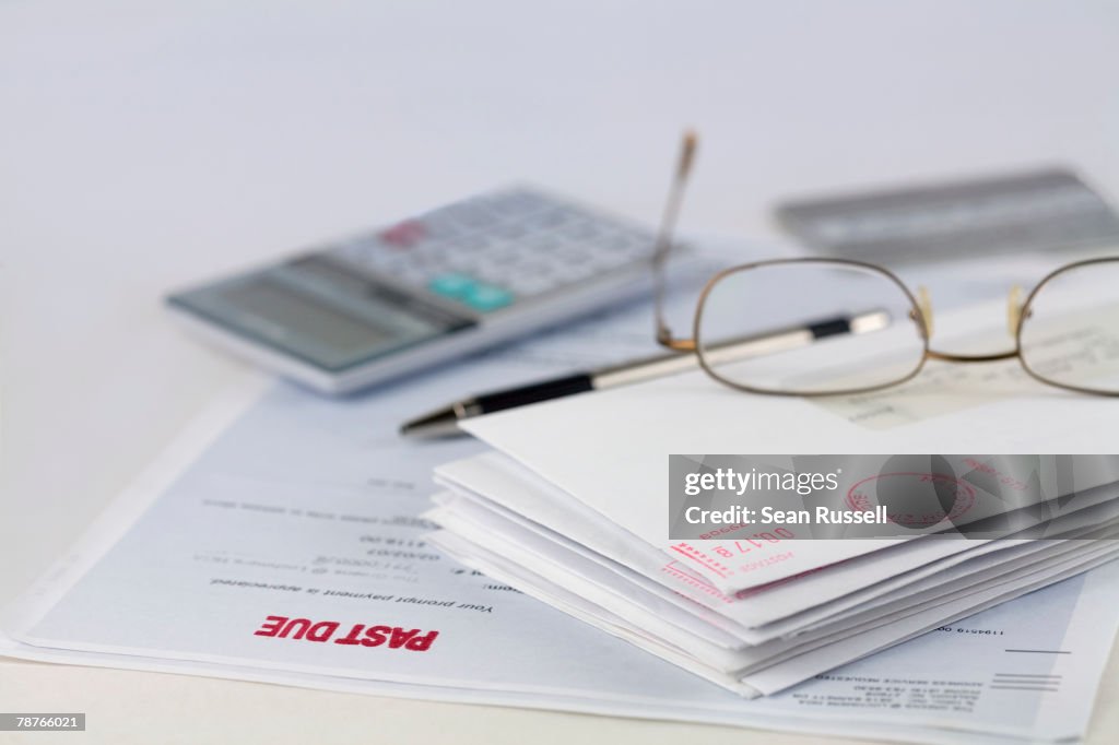 Stack of envelopes with pen, calculator, glasses and credit card