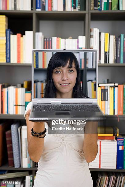 a young woman holding a laptop in front of her face - hiding behind laptop stock pictures, royalty-free photos & images