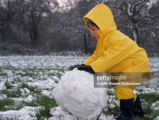 a young boy making a snowman - レインコート ストックフォトと画像