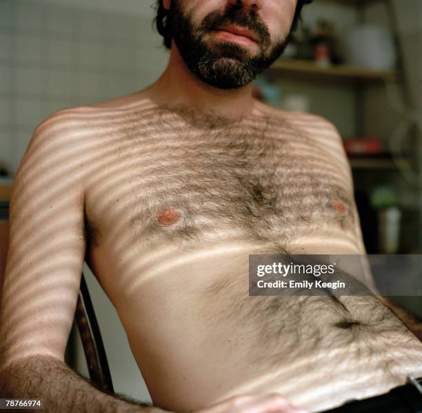 a semi-dressed man sitting on a chair - brusthaare stock-fotos und bilder