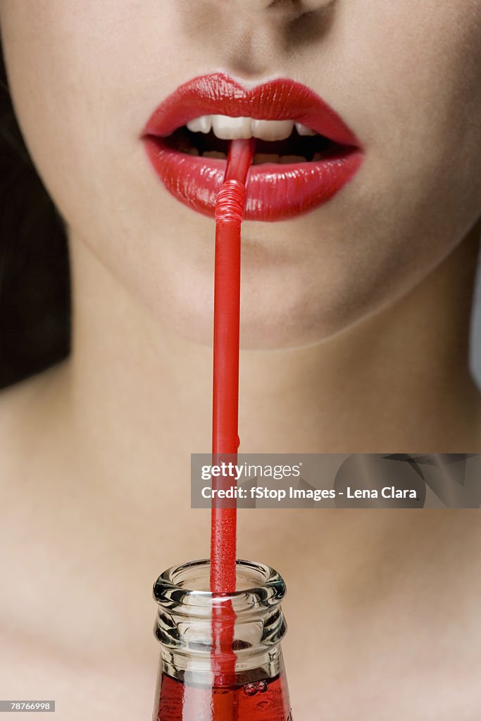 A woman wearing red lipstick drinking from a red straw