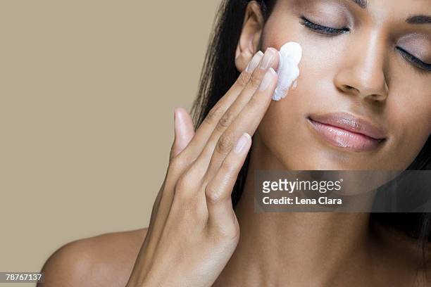a woman rubbing moisturizer into her skin - woman skin face stock-fotos und bilder