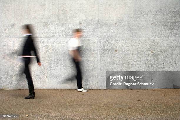 two people walking past a wall - passing stock pictures, royalty-free photos & images