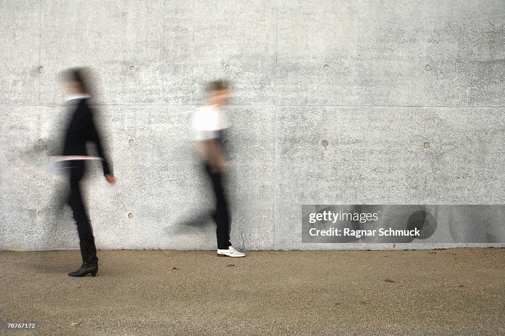 Two people walking past a wall