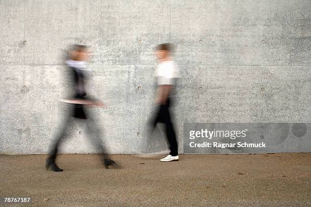 two people walking past a wall - moving past ストックフォトと画像