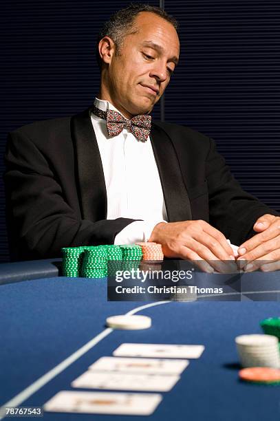 well dressed man peeking at hand of cards at casino table - gaming casino stock-fotos und bilder