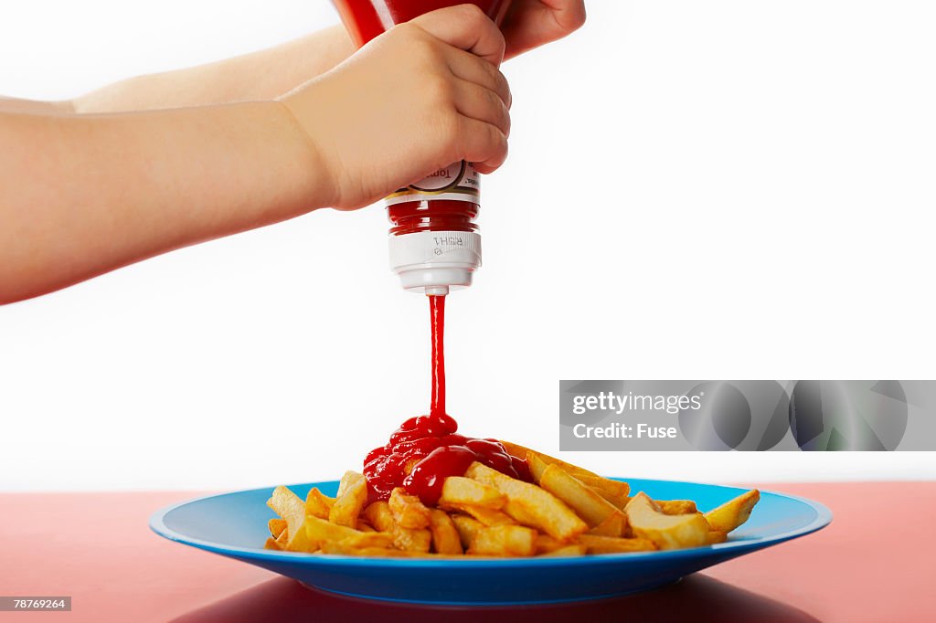 Child Squeezing Ketchup on French Fries