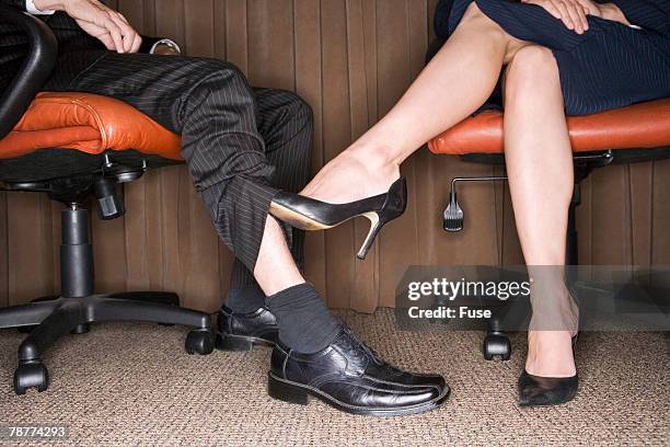 woman playing footsie with businessman - playing footsie stock-fotos und bilder