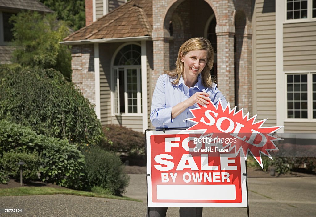 Woman Removing Sold Sign in Front of New House