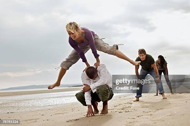 young friends playing leapfrog on beach - bockspringen stock-fotos und bilder
