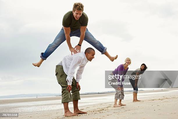young friends playing leapfrog on beach - bockspringen stock-fotos und bilder