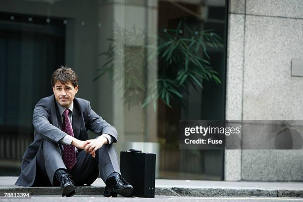 sad businessman sitting on kerb outside office building - kerb stock-fotos und bilder