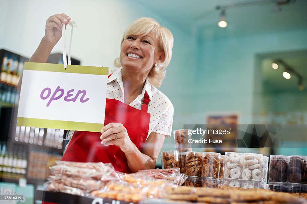 Owner Hanging Open Sign in Delicatessen Window