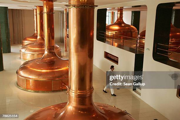 Worker walks past the giant copper vats that contain the brew of heated barley mash, known as wort, mixed with hops that will become Pilsner-Urquell...