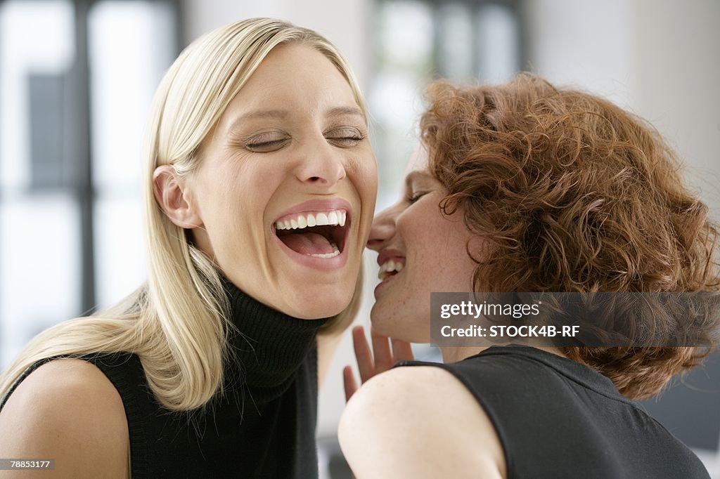 Two laughing young women whispering