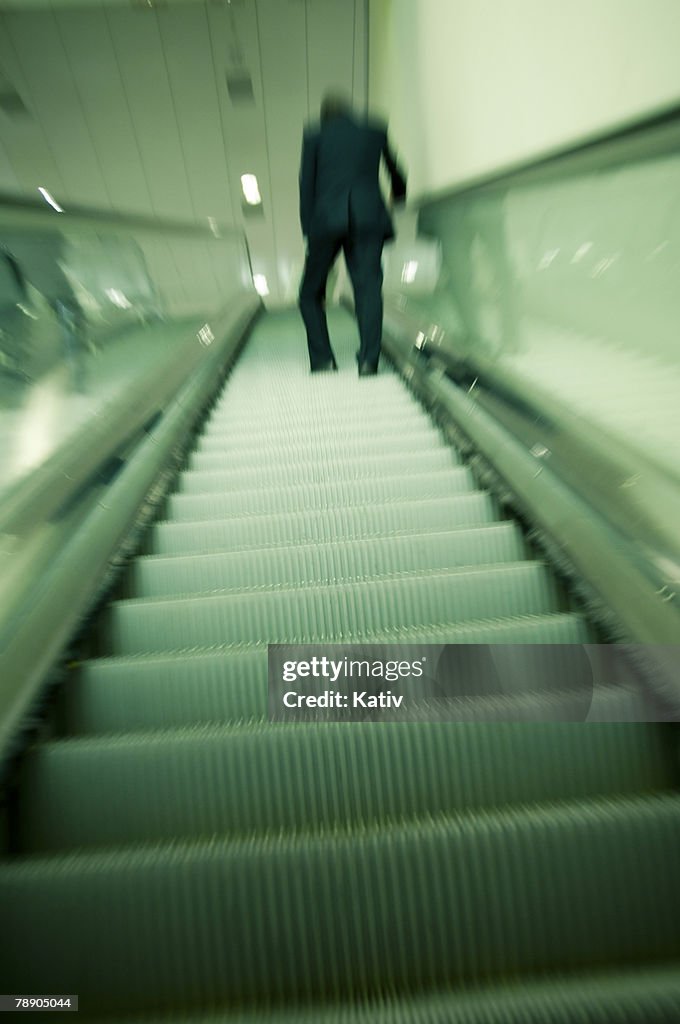 Rather tired looking man going up on Airport escalator, rear view. Blurred shot is intentional to give dramatic feeling.
