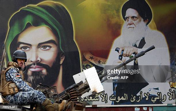 An Iraqi police commando monitors the area as he sits on top of a militray vehicle infront of huge portraits of revered Shiite cleric Mohammed Sadeq...