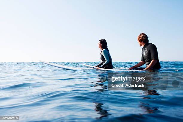 couple sitting on surfboards in the water. - sitting on surfboard stockfoto's en -beelden