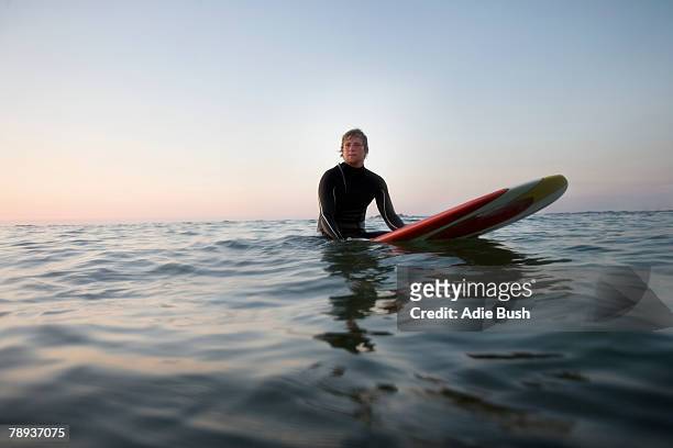 man sitting on surfboard in the water. - surfer wetsuit stockfoto's en -beelden