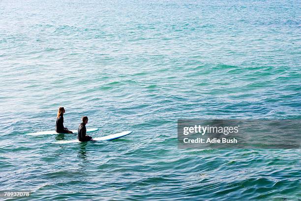 couple sitting on surfboards in the water. - bay of water fotografías e imágenes de stock