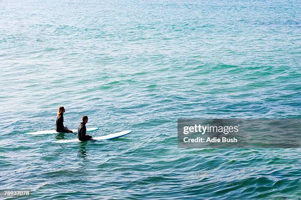 couple sitting on surfboards in the water. - wetsuit stock pictures, royalty-free photos & images