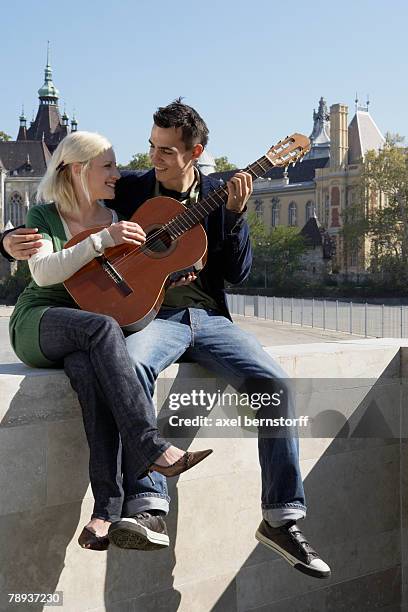 couple playing guitar outdoors smiling. - vajdahunyad castle stock pictures, royalty-free photos & images