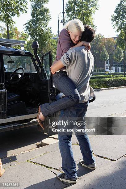 couple embracing by an suv smiling. - axel jump fotografías e imágenes de stock