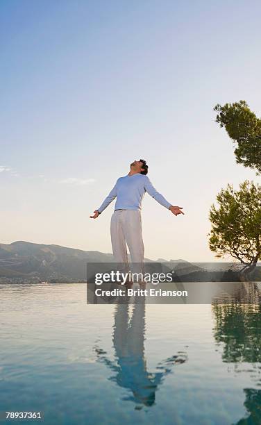 man stands in open space sky and reflective pool arms out. - open arms stock-fotos und bilder