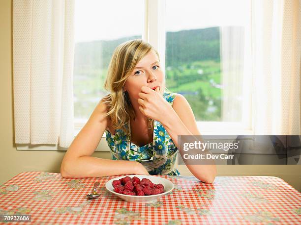 woman eating bowl of raspberries at table. - fruit bowl stock pictures, royalty-free photos & images