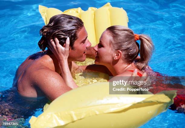 Stock Picture, Elevated view of a couple embracing and looking into each others eyes, whist being supported on a yellow inflatable bed in a swimming...