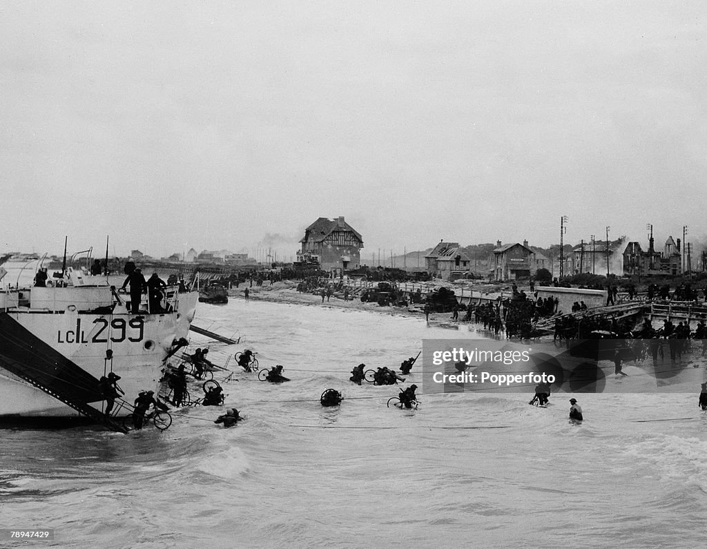 War & Conflict. World War Two. France 6th June 1944. Allied infantry army units wade ashore from landing craft to one of the beaches in Normandy on D Day. Many of the troops and soldiers are carrying bicycles with them.