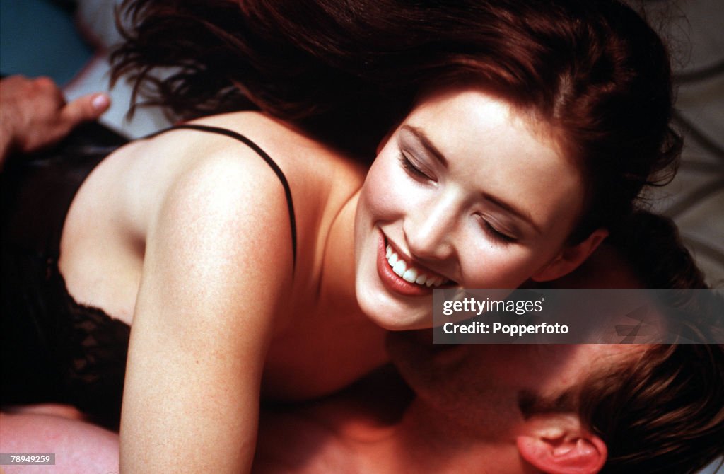 Stock Photography. Young partly dressed couple enjoying a passionate embrace in bed.