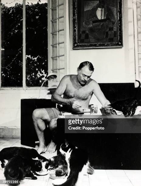 Literature Personalities, pic: circa 1940's, Author Ernest Hemingway pictured at breakfast with a group of cats feeding at his feet, Ernest...