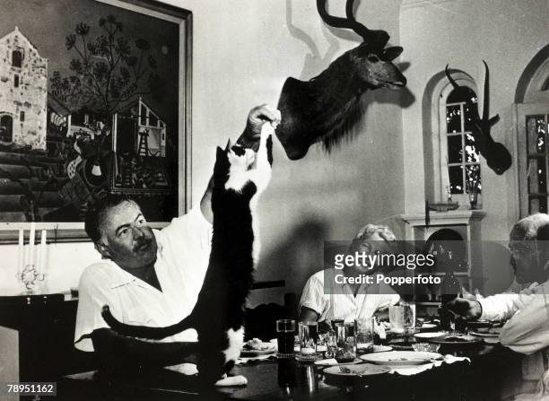 Literature Personalities, pic: circa 1946, Author Ernest Hemingway watched by his wife Mary Welsh Hemingway , feeds tit bits to the cat at dinner....