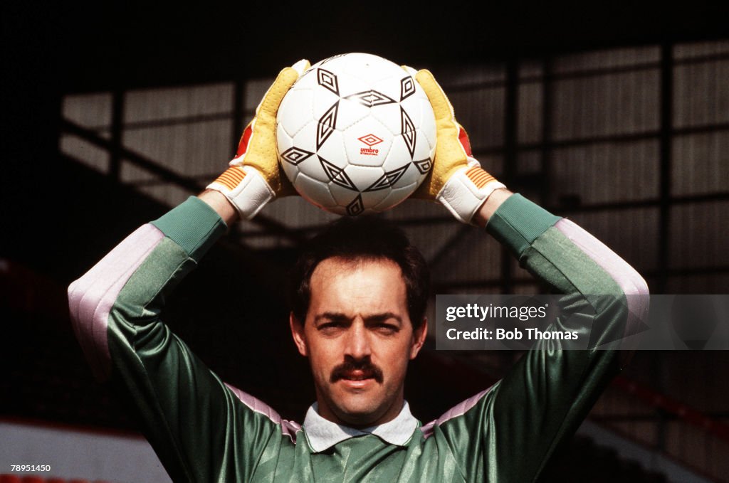 Liverpool goalkeeper Bruce Grobbelaar holds a ball above his head as he poses for the camera.
