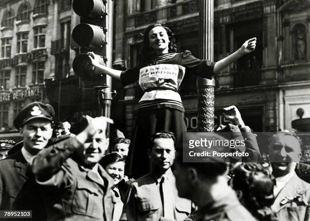 Young woman wearing the front cover of the Evening News is held aloft by Allied servicemen as the West End of London celebrates the end of conflict...