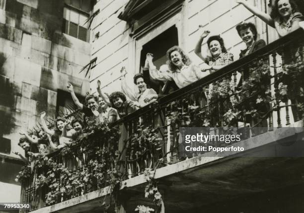Group of young women office workers shout and cheer from a balcony as they celebrate Victory in Europe Day to mark the end of European conflict in...