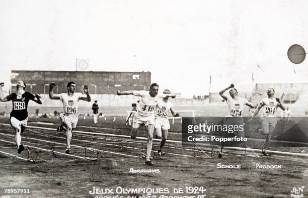 Harold Abrahams of Great Britain breaks the tape to finish in first place to win the gold medal ahead of 2nd placed silver medallist Jackson Scholz...