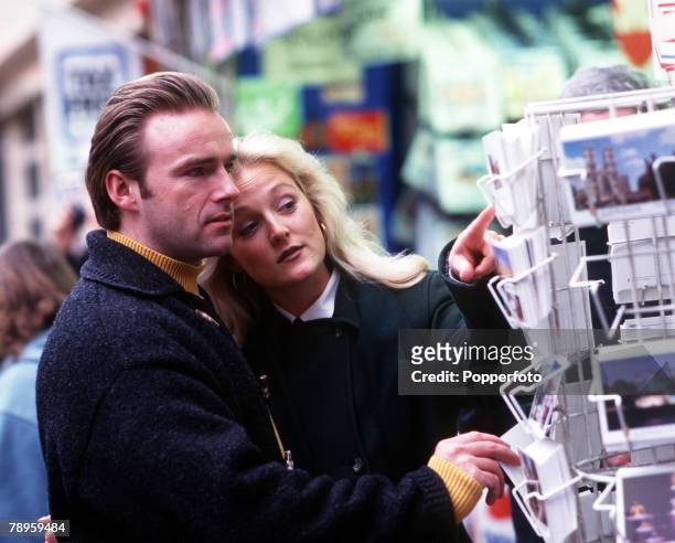 Young couple choosing post cards from a rack outside a shop in London